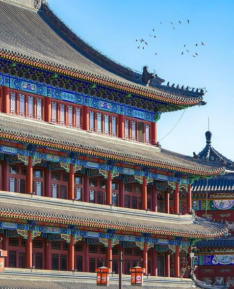 A traditional Chinese building with ornate blue and red decorations, a tiled roof, and a statue on the roof. 2