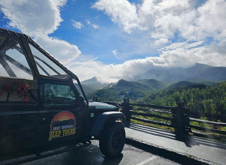 A black SUV with 'Smoky Mountains Jeep Tours' on its side parked on a road with a scenic view of mountains and clouds. 1