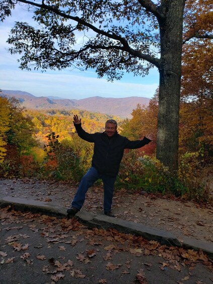 A person standing on a path with autumn foliage and a mountainous landscape in the background. 4
