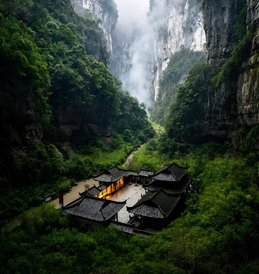 A traditional Chinese building nestled in a lush valley between steep cliffs. 2