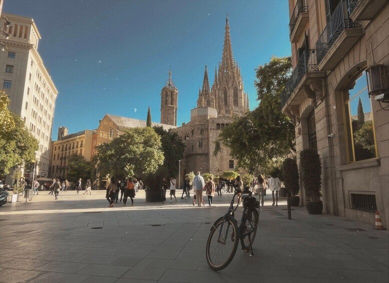 A plaza with people walking, a bicycle, and historic buildings with spires. 3