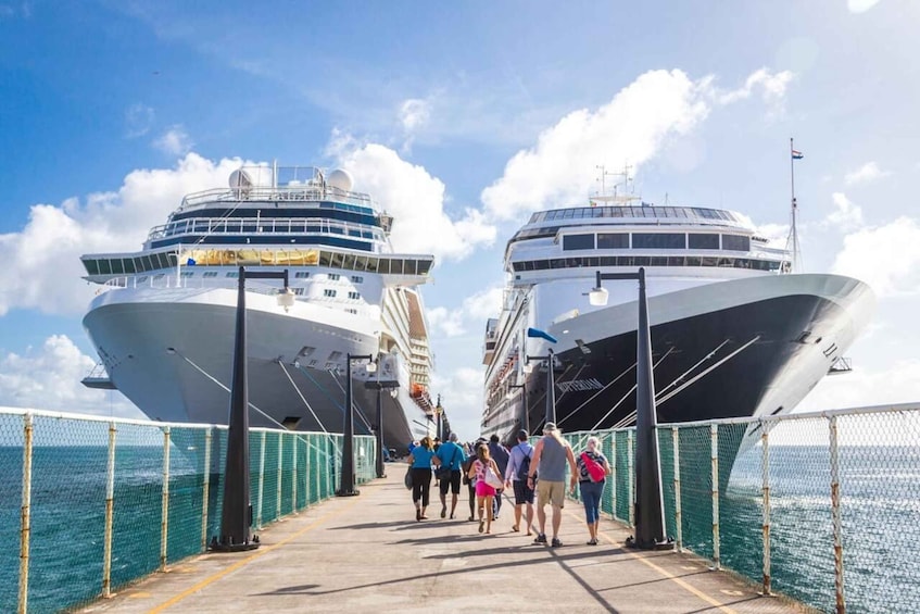 Two large cruise ships docked at a port with people walking on the pier. 1