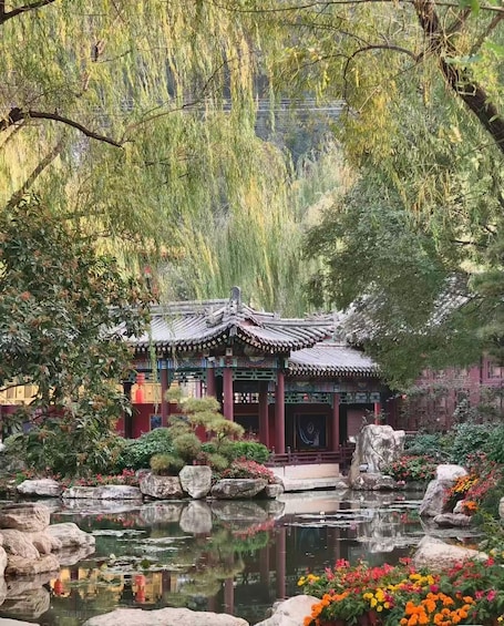 A traditional Chinese pavilion surrounded by a pond with rocks and colorful flowers. 2
