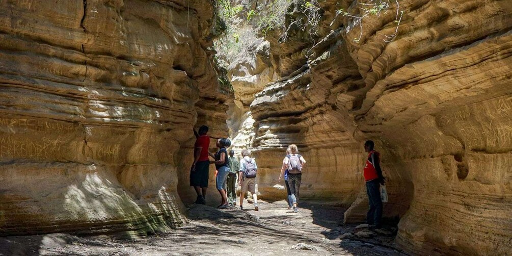 A group of people hiking through a narrow canyon with layered rock formations. 3