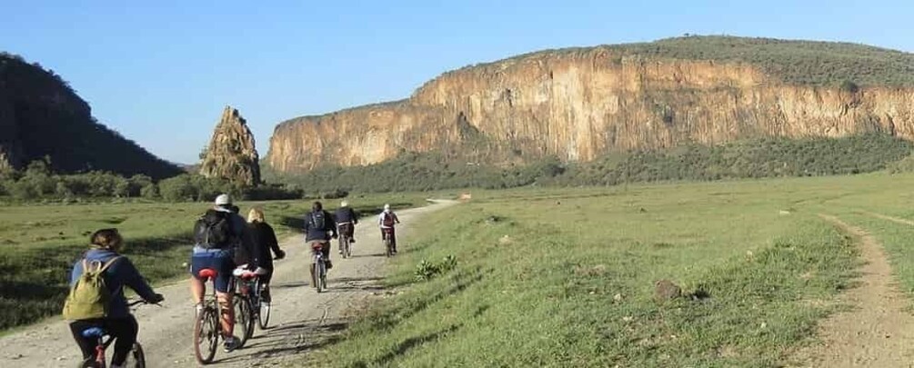 A group of cyclists on a dirt path with a large cliff in the background. 1