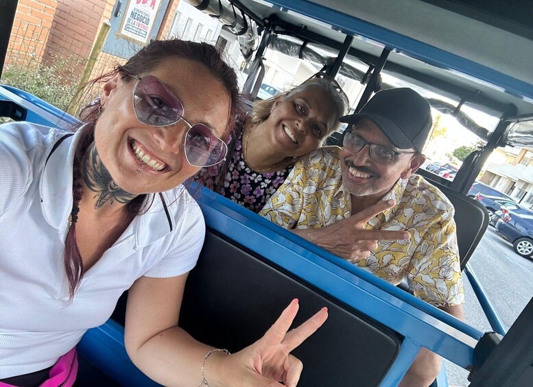 Three people in a vehicle with a blue interior, a brick building, and a sign in the background. 5