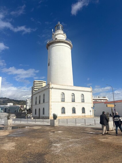 A white lighthouse with a cylindrical tower and a dome on top, situated next to a white building with arched windows. 4