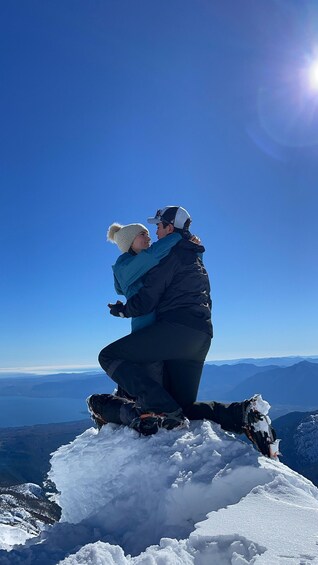 Two people embracing on a snowy mountain peak with a clear sky and distant mountains. 5