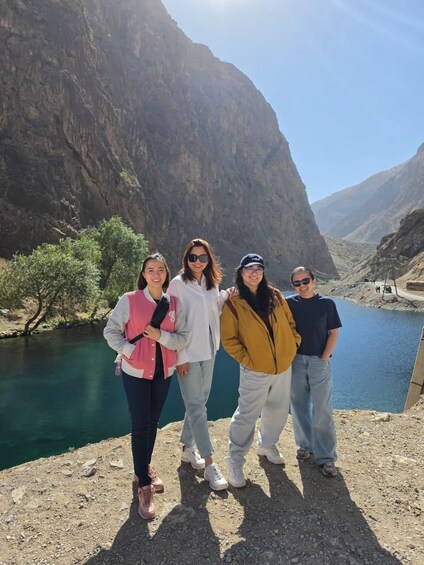 Four people standing by a river with a mountainous backdrop. 3