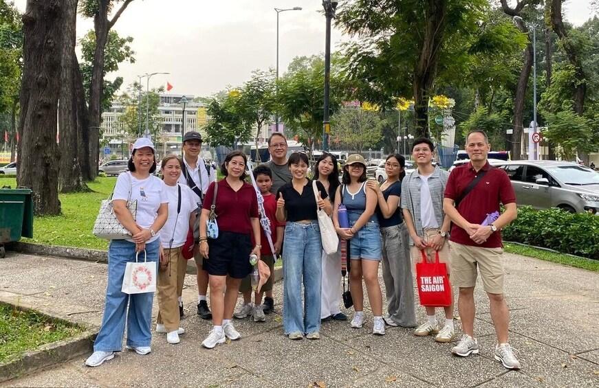 A group of people standing on a sidewalk with trees and buildings in the background. 2