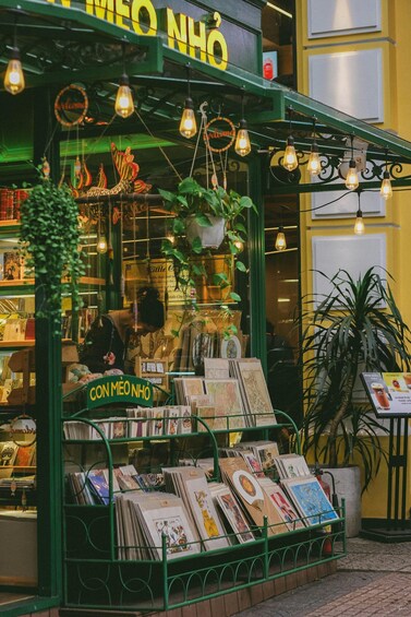 A bookstore with a green facade, hanging light bulbs, and a sign that reads 'CON MEO NHÔ'. 4