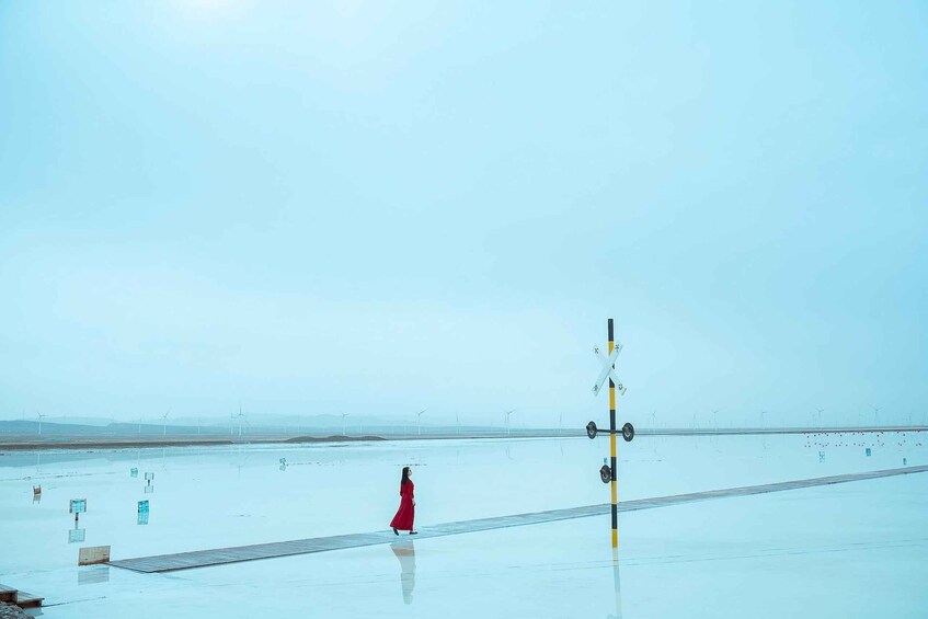 A woman in a red dress walking on a reflective surface with wind turbines in the background. 1