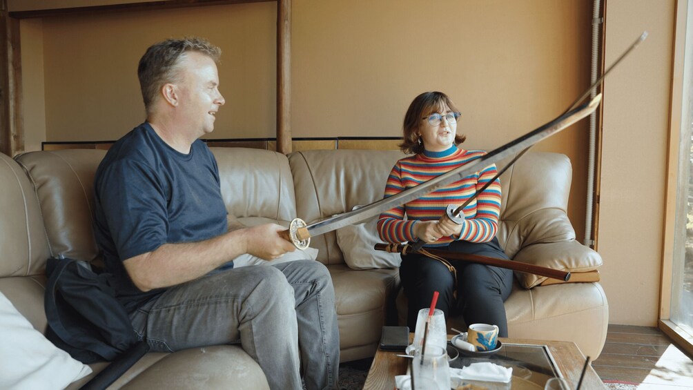 Two people sitting on a couch, one holding a sword. 1