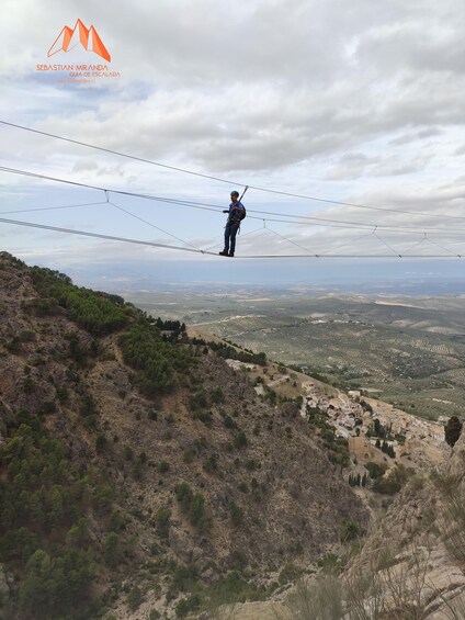 A person walking on a suspended bridge with a mountainous landscape in the background. 4