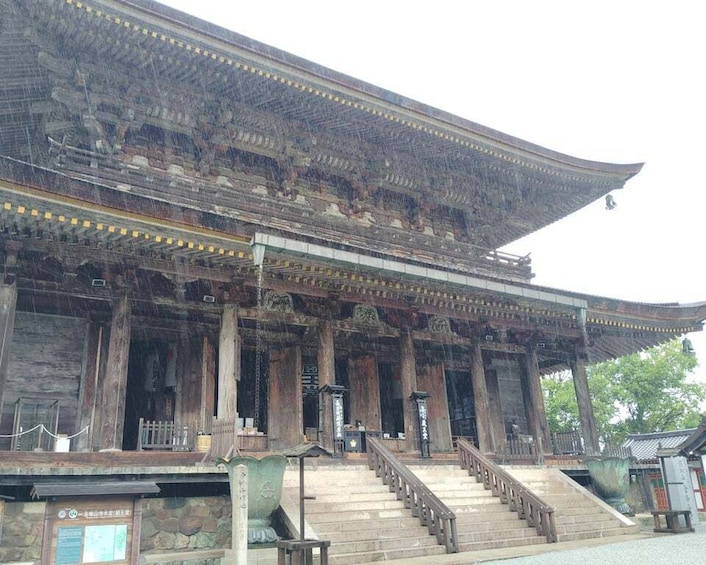 A traditional wooden building with a steeply pitched roof and a staircase leading up to the entrance. 2