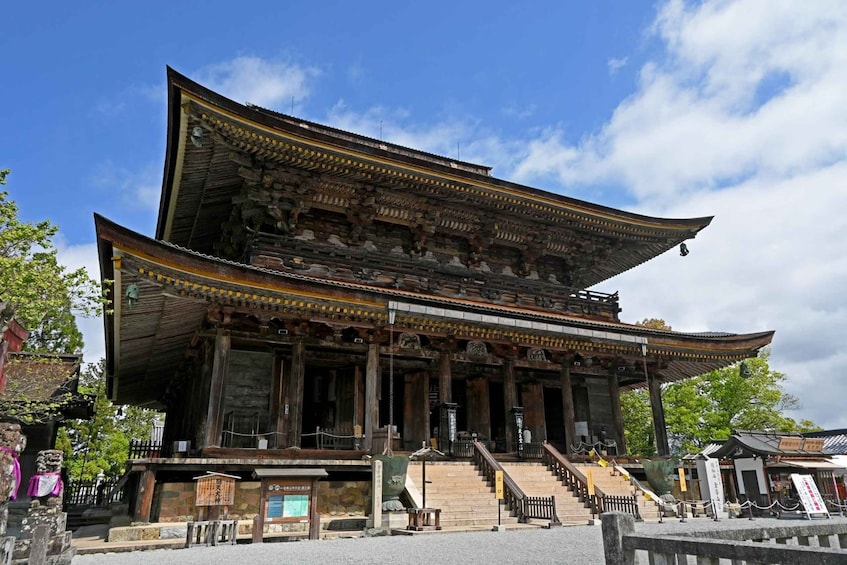 A traditional wooden building with a curved roof, stone steps leading up to the entrance, and a clear blue sky in the background. 1
