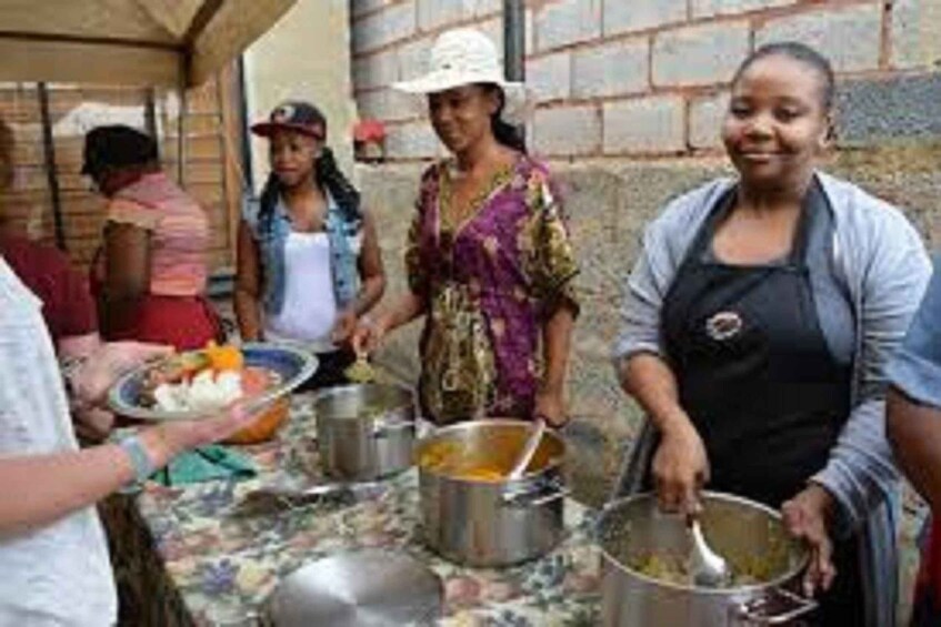People serving food at an outdoor event with tables and pots. 1