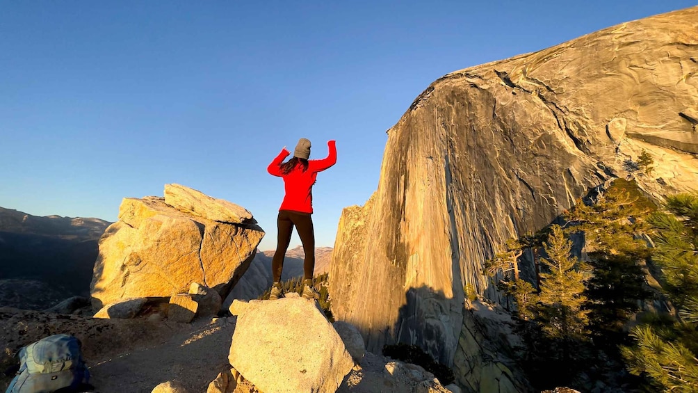 A person standing on a rocky outcrop with a large cliff in the background. 5