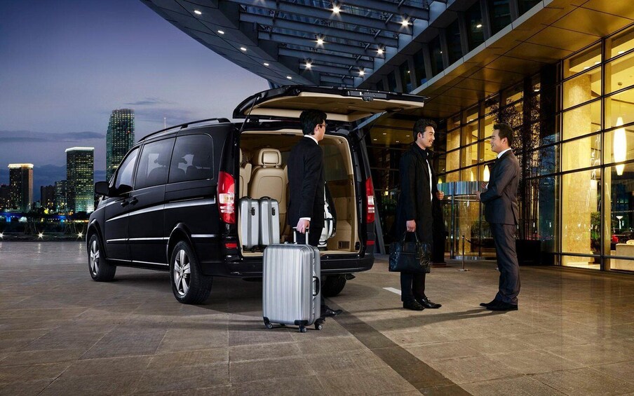 A black van with its back doors open, luggage inside, and two men standing beside it. 4