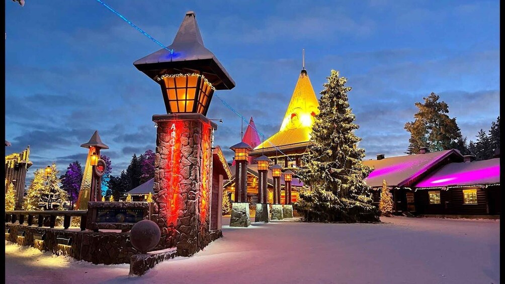 A snow-covered landscape with a brightly lit building featuring a conical roof and a large Christmas tree. 5
