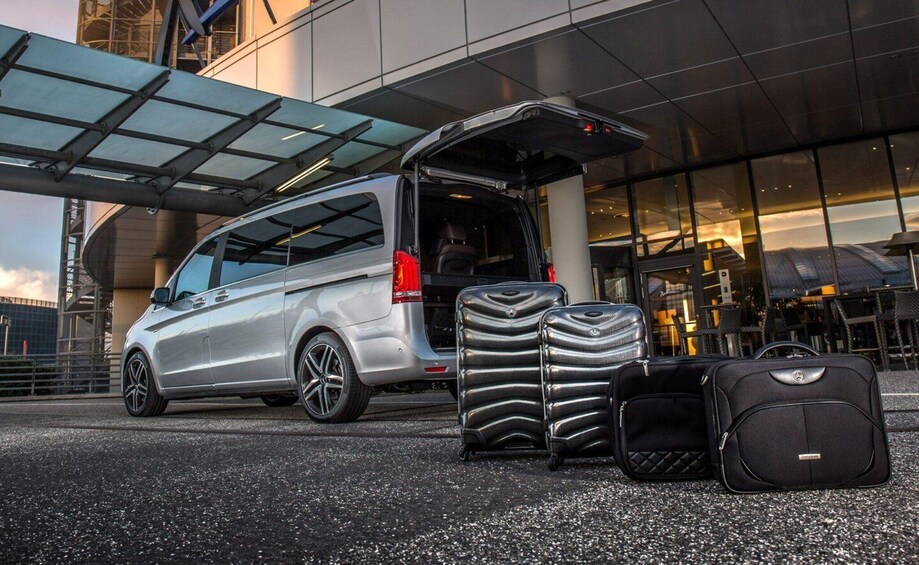 A silver van parked in front of a building with its trunk open, displaying three suitcases. 3