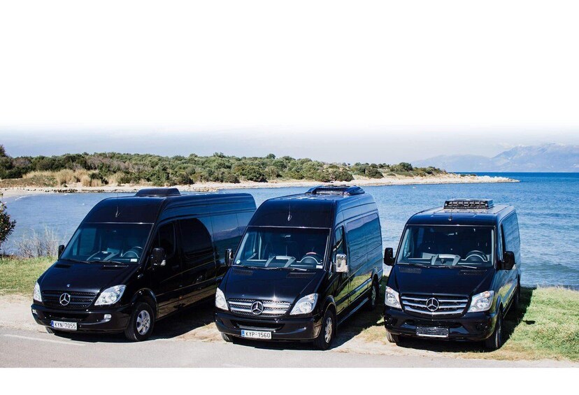 Three black Mercedes vans parked by a coastal road with a view of the sea and distant mountains. 1