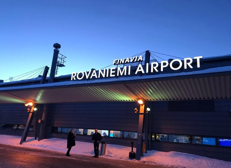 The Rovaniemi Airport sign at dusk with two people standing below. 2