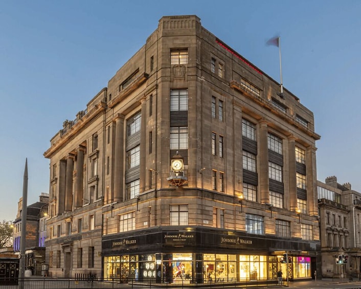 A historic building with 'Johnnie Walker' signage, large windows, and a flag on top. 1