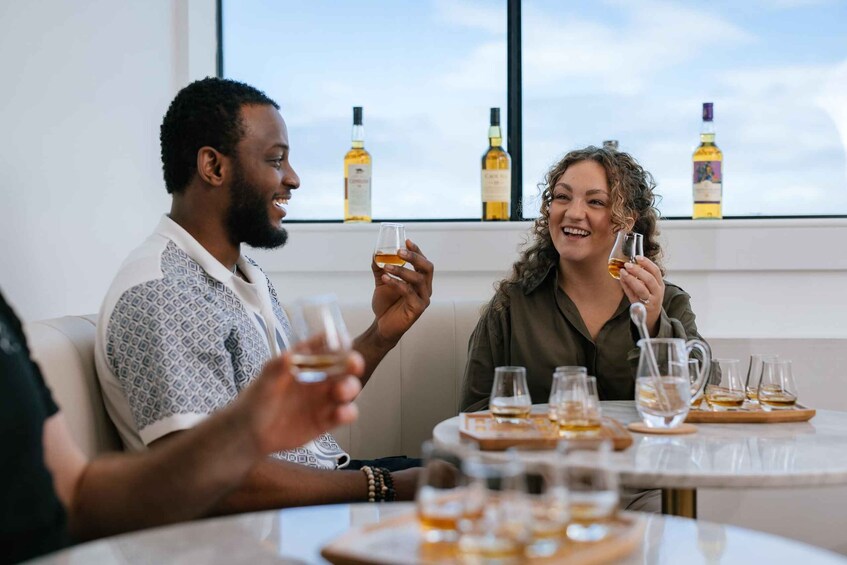 Two people sitting at a table with glasses of whiskey and a window with bottles in the background. 5