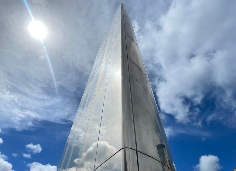 A tall, slender structure with a reflective surface, set against a blue sky with scattered clouds. 1