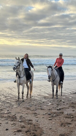 Two people riding horses on a beach with the ocean in the background. 4