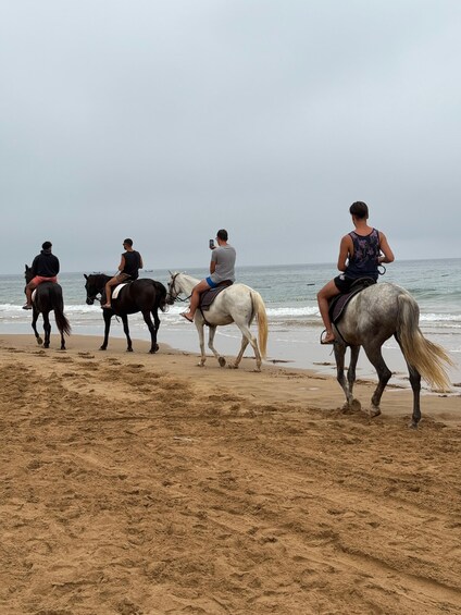 Four people riding horses along a sandy beach with the ocean in the background. 2