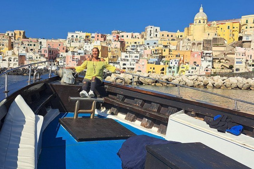 A boat with a person on deck, a blue deck, and colorful buildings in the background. 1