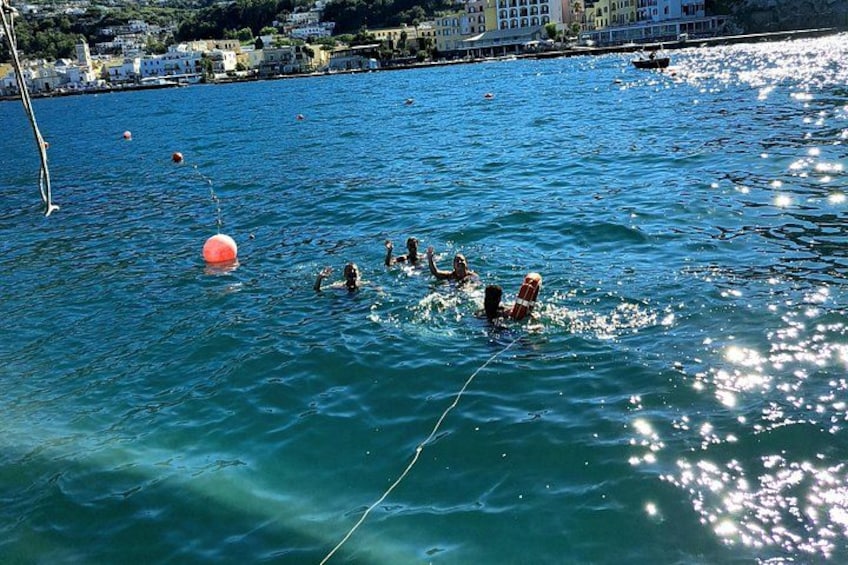 People swimming in a body of water with a buoy and buildings in the background. 2