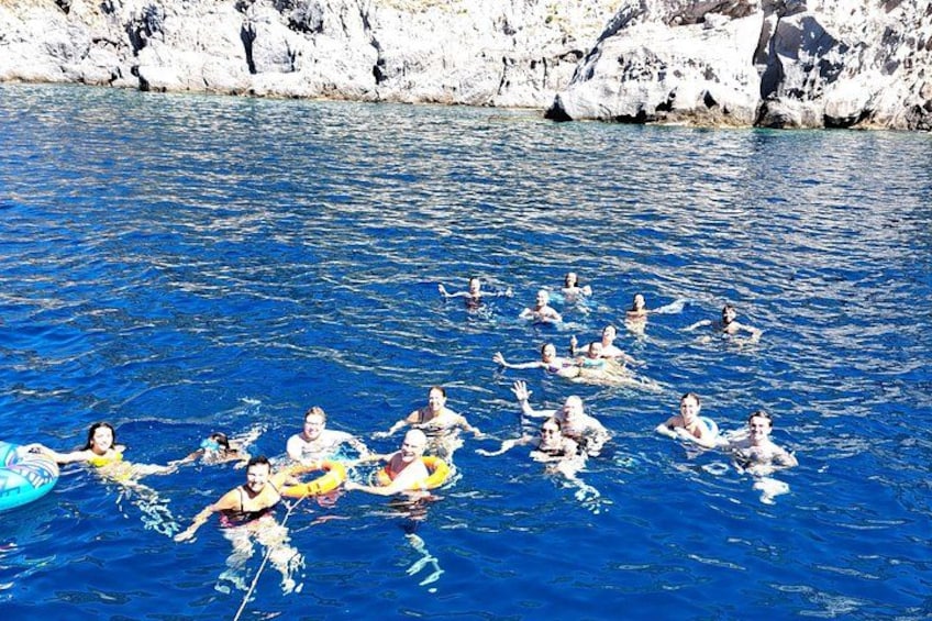 A group of people floating on the water with a rocky coastline in the background. 3