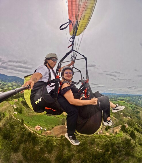 Two people paragliding over a lush green landscape with rolling hills and a cloudy sky. 3