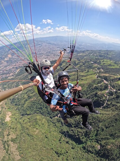 Two people paragliding with a cityscape and green hills in the background. 3