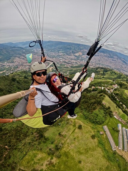 Two people paragliding over a cityscape with green hills below. 2