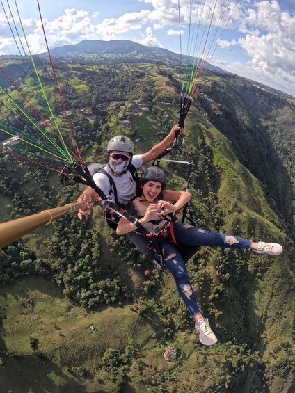 A person paragliding over a mountainous landscape with lush greenery and scattered buildings. 1