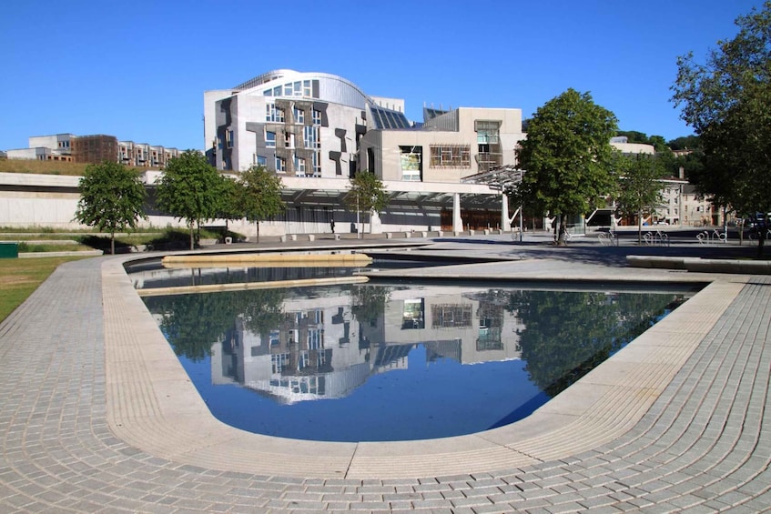 A modern building with a curved facade, a reflective pool, and surrounding trees. 1