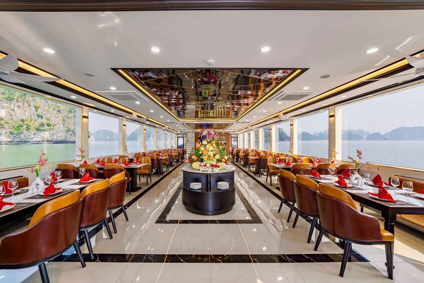 A cruise ship dining area with tables set for a meal, a central floral arrangement, and a view of the sea. 2