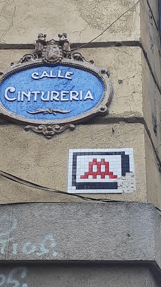 A blue street sign with 'Calle Cintureria' and a pixelated red and black sign below it. 5