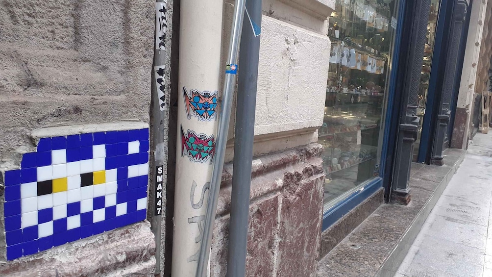 A building corner with a blue and white checkered pattern, a metal pole with stickers, and a glass storefront. 3