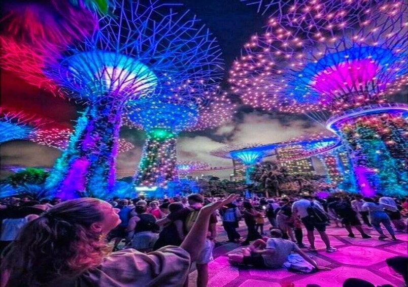 A crowd gathered around illuminated structures with a large, colorful display in the background. 1