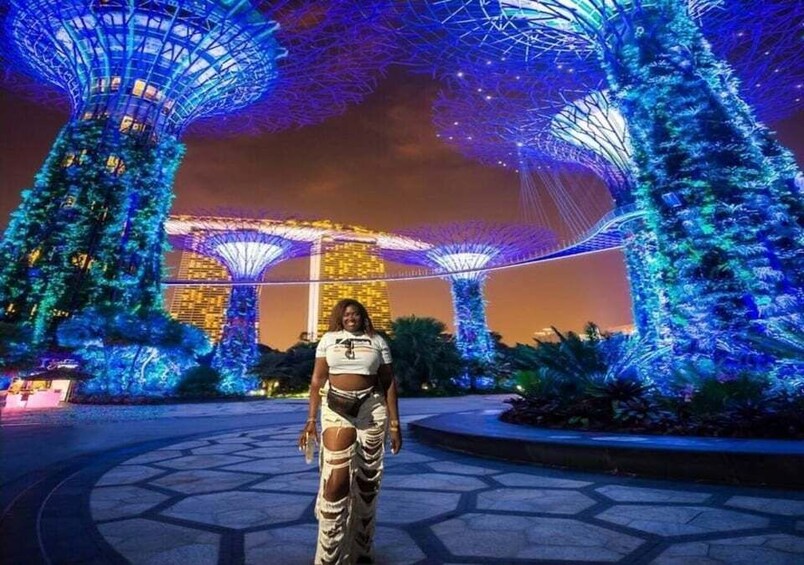 A person standing in front of a large illuminated structure with a distinctive roof design, surrounded by trees and a building with a unique architectural style. 4