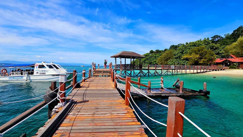 A wooden pier leading to a small island with a thatched-roof structure, surrounded by clear turquoise waters and lush greenery. 4