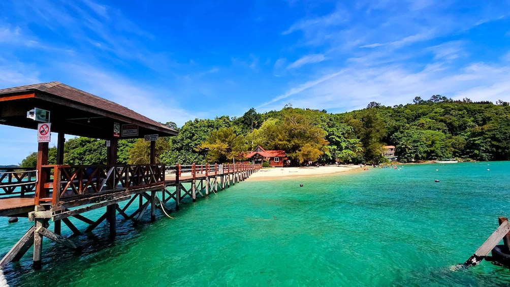 A wooden pier extending into turquoise waters, a beach, and a forested hill in the background. 2