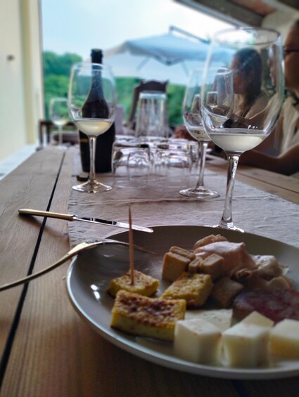A wooden table with a plate of cheese cubes, wine glasses, and a bottle of wine. 5