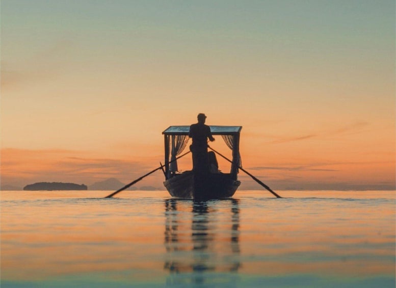 A person in a boat with a canopy, paddling on calm water during sunset. 1