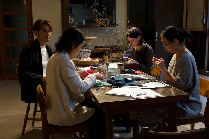 Four people sitting at a wooden table with various craft materials and a basket of items. 3